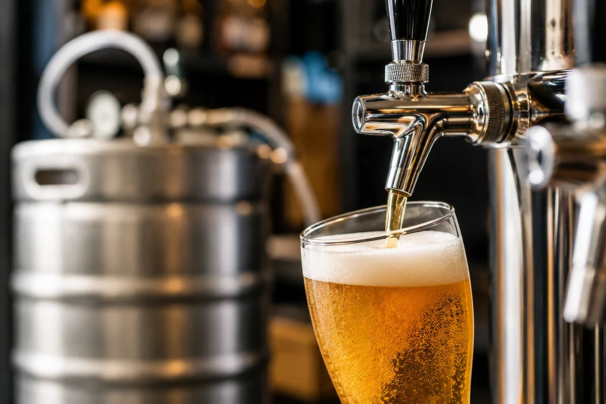 Cerveza servida desde un grifo profesional con barril desenfocado al fondo en una instalación de dispensación - Install Beer